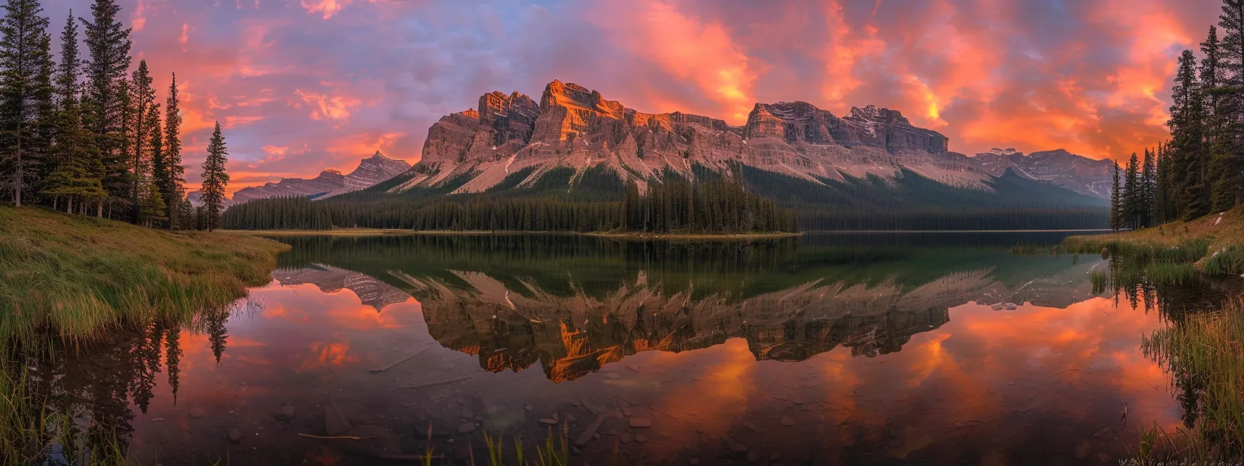 a breathtaking sunset casts vibrant orange and pink hues over a tranquil lake, reflecting the dramatic skyline of distant mountains under a clear sky.