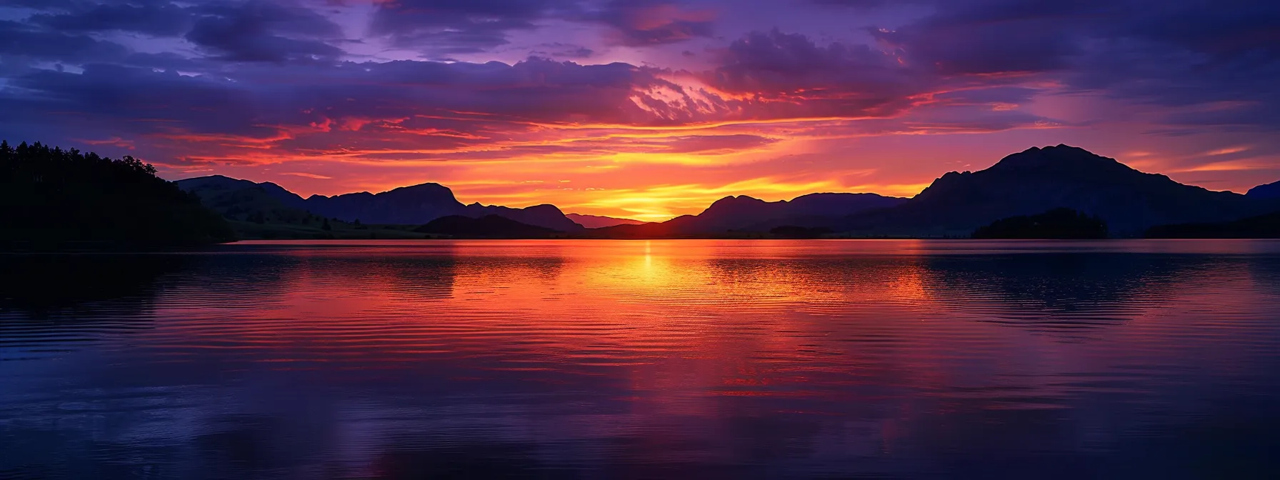 a breathtaking sunset casts vibrant hues of orange and purple across a serene lake, with silhouettes of distant mountains reflecting in the calm waters.