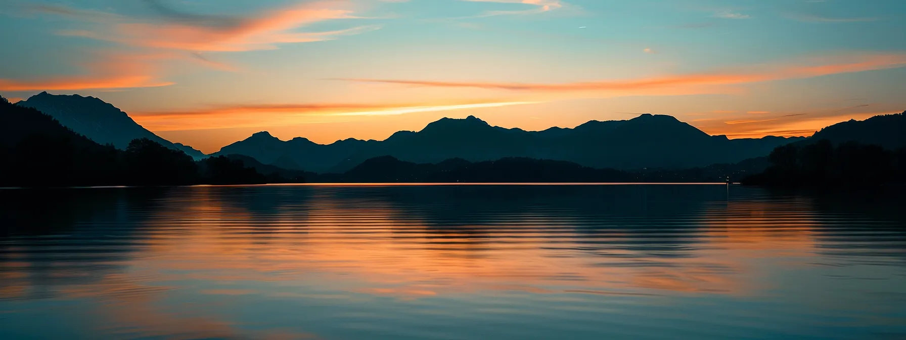 a vibrant sunset casts a warm glow over a serene lake, with silhouetted mountains rising majestically in the background, creating a peaceful and captivating atmosphere.